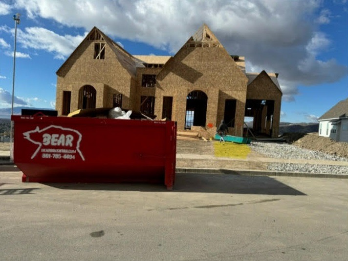 A red Bear Services roll-off bin parked at a house under construction